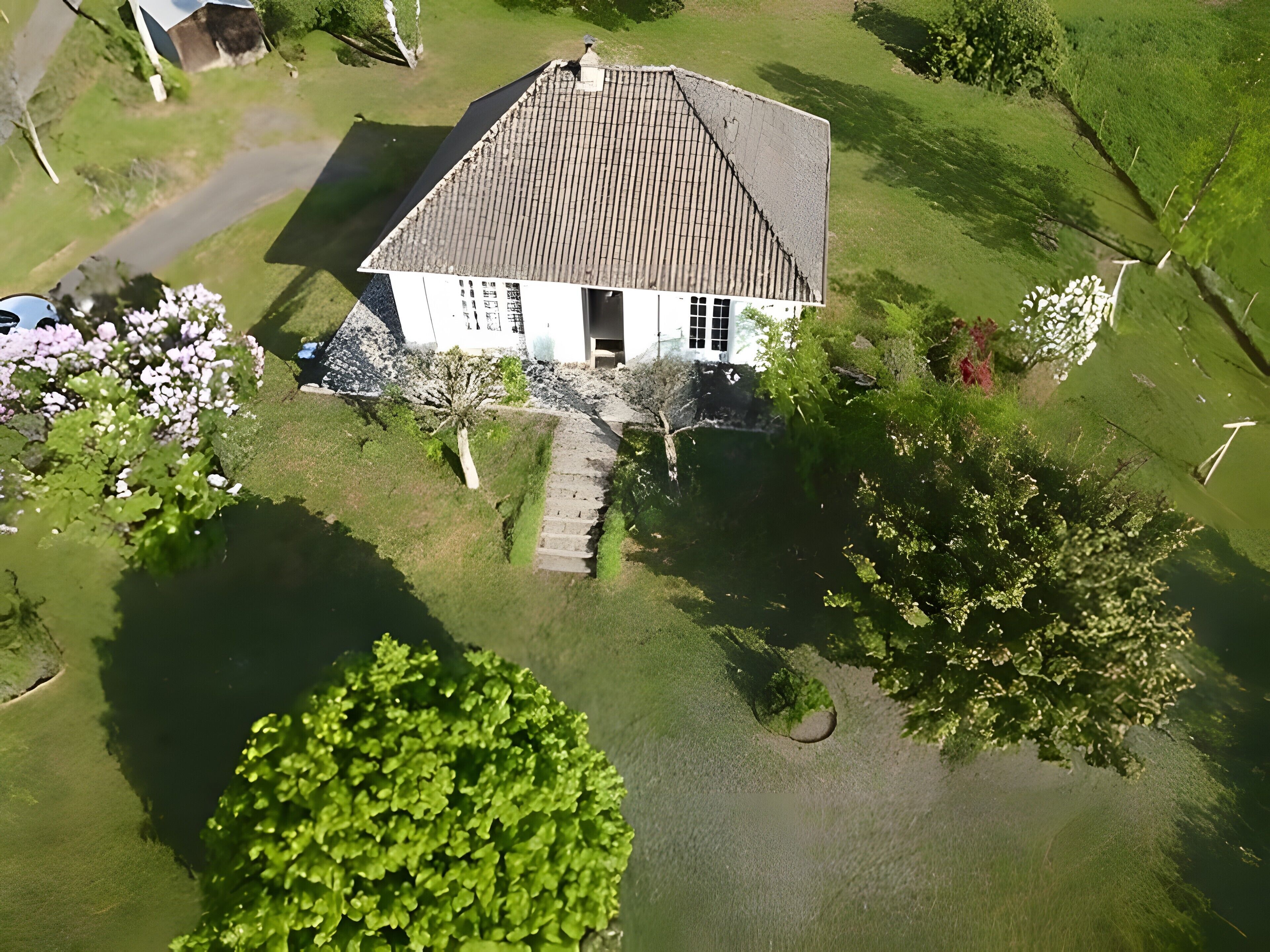 Luchtbeeld van een huis met schuin dak, een veranda en een kleine tuin.