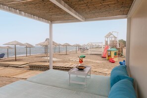 Ein Zimmer direkt am Strand mit Meerblick, einem Spielbereich und einem Tisch mit einem Getränk.