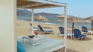 Ett rum vid stranden med en säng, ett bord med en drink på och utsikt över stranden och havet.