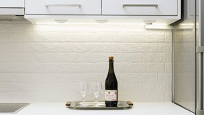 Une cuisine avec des armoires blanches, un plan de travail en bois, une bouteille de vin et des verres.