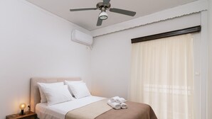 Un lit bien fait, recouvert d’une couverture beige et marron, avec une lampe de chevet et un ventilateur de plafond.