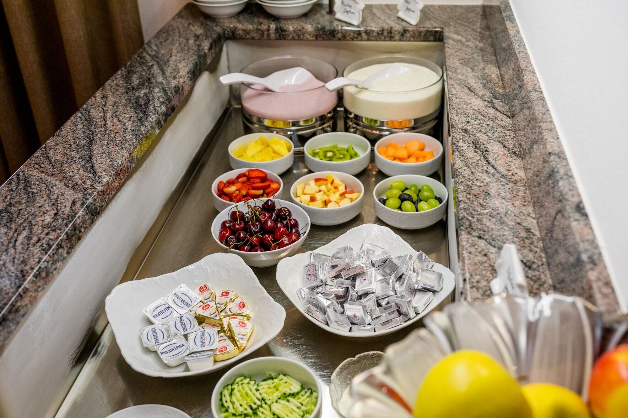 A buffet spread with various fruits, cheeses, and packaged snacks.