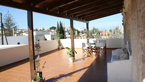 En overdækket terrasse med træloft, flisegulv og et siddeområde med stole og bænk.