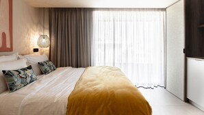 Quarto de hotel com cama, cortinas, luminária na parede e uma janela grande.