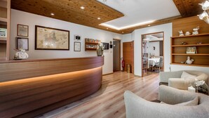 A reception area with a wooden reception desk, framed certificates, a map, and a modern chandelier. - Room 'Passerblick Silber Zimmer 3' with Mountain View, Shared Pool and Wi-Fi (Tirolo)