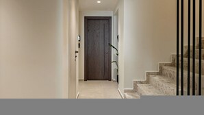 Ein Flur, der zu einer Holztür führt, eine Treppe mit schwarzen Geländern und ein Blumentopf.