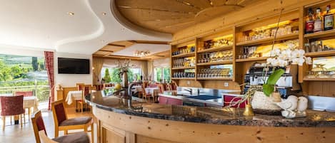 A bar area with a curved counter, wooden shelves with glassware, and a view of the outdoors.