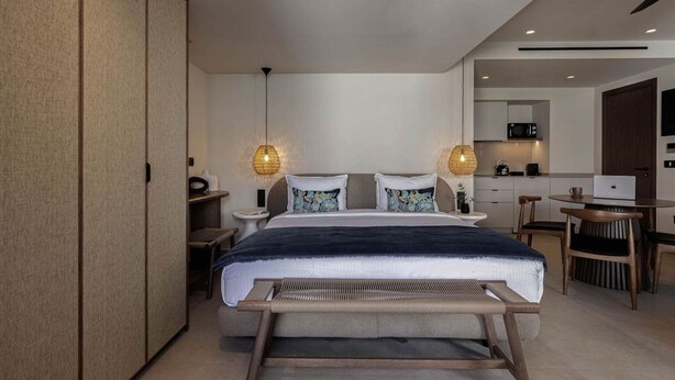 Ein modernes Hotelzimmer mit Bett, Nachttischen, einem Schreibtisch und einer Küchenzeile.