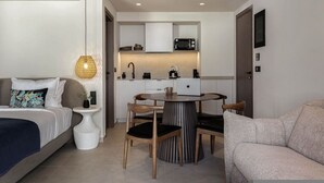 Ein kleines Hotelzimmer mit Bett, Esstisch mit Stühlen, Küchenzeile und einer Sitzecke.