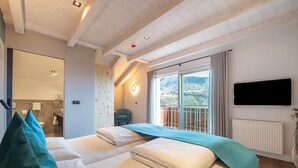 Quarto com duas camas, televisão, porta de correr para uma varanda e vista para montanhas.