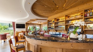 Uma área de bar com balcão curvo, prateleiras de madeira com copos e vista para o exterior.