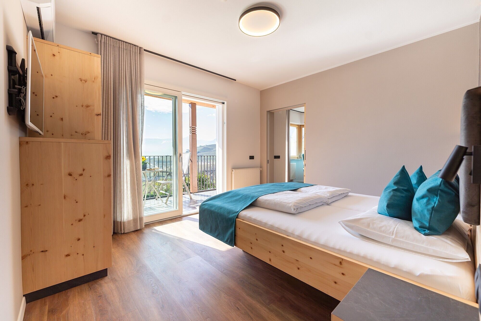 Et soveværelse med seng, træskab, balkon med udsigt og en loftlampe.