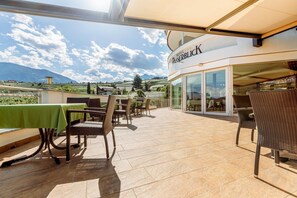 Eine Hotelterrasse mit Tischen und Stühlen, ein Glastür-Eingang und Blick ins Grüne.
