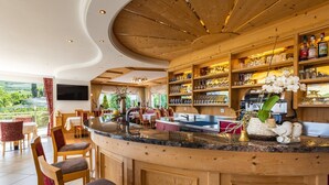A bar area with a curved counter, wooden shelves with glassware, and a view of the outdoors. - Room 'Passerblick Suite 4' with Mountain View, Wi-Fi and Air Conditioning (Tirolo)