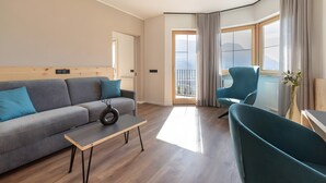 A modern living room with a sofa, a coffee table, and a chair. There is a large window with curtains, a door, and a view of the outdoors. - Room 'Passerblick Suite 4' with Mountain View, Wi-Fi and Air Conditioning (Tirolo)