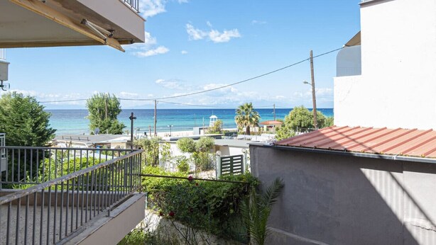 Un balcón con vista al mar, un edificio con techo rojo y algo de vegetación.