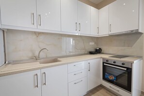 A modern kitchen with white cabinets, a sink, a stove, and a coffee maker. - Sabbia Seafront Apartment 4 by RentalsPro (Nea Moudania)