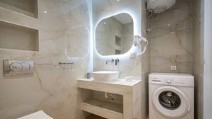 Un baño con tocador de mármol, lavamanos, espejo con iluminación, inodoro y lavadora.