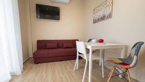 Una habitación con un sofá rojo, una mesa blanca con una silla y un televisor montado en la pared.