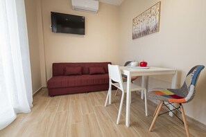 A room with a red sofa, a white table with a chair, and a TV mounted on the wall. - Sabbia Seafront Apartment 4 by RentalsPro (Nea Moudania)