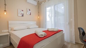 Habitación de hotel con cama, manta roja, almohadas blancas, una silla y una obra de arte en la pared.