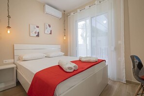 A hotel room with a bed, a red blanket, white pillows, a chair, and artwork on the wall. - Sabbia Seafront Apartment 4 by RentalsPro (Nea Moudania)