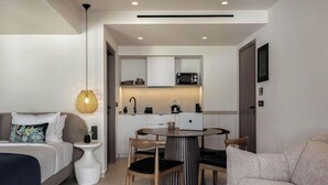 Una habitación de hotel compacta con cama, una pequeña mesa de comedor, sillas, kitchenette y una pared blanca con una puerta.