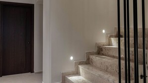 Una escalera con barandilla, una puerta con diseño de vetas verticales de madera e iluminación empotrada.