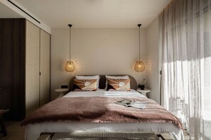 Ein Schlafzimmer mit einem großen Bett, zwei Nachttischen, einem Beistelltisch und einem Fenster mit durchsichtigen Vorhängen.