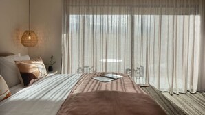 A bedroom with a bed, a bedside table, a lamp, and sheer curtains.