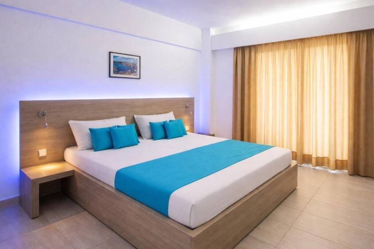 Ein modernes Hotelzimmer mit einem großen Bett, einem Nachttisch, einem Wandbild und einem Fenster mit Vorhängen.