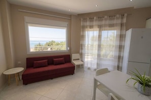 Ein Zimmer mit einer Couch, einem Esstisch, einem Stuhl, einem kleinen Tisch, einem Kühlschrank und einem Fenster mit Blick.