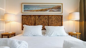 Ett hotellrum med en stor säng, två sänglampor, en dekorativ sänggavel, en inramad tavla ovanför sängen och hoprullade handdukar på sängen.
