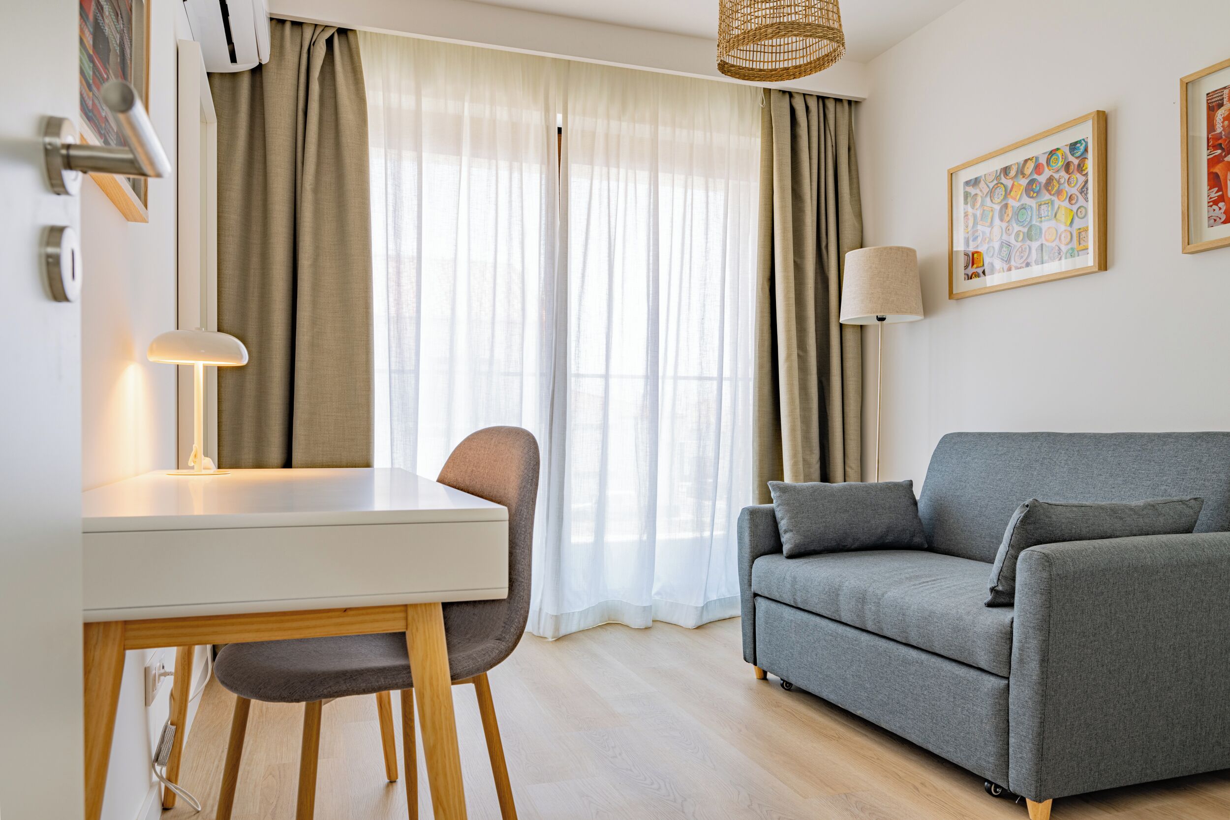 Ein modernes Wohnzimmer mit weißem Schreibtisch, grauem Sofa und Essbereich.