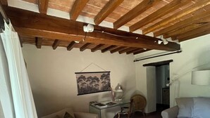 A cozy room with a wooden ceiling, a sofa, a bed, a glass table, and a chair. - Hidden Tuscan Gem- surrounded by rolling hills. Charming villa, sleeps up to 6. (Caprese Michelangelo)
