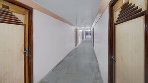Un pasillo largo y estrecho con puertas de madera a ambos lados, letreros con números encima de las puertas y piso de baldosas.