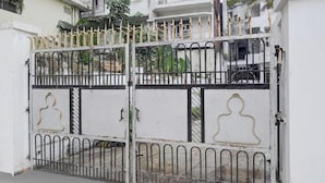 Una entrada protegida por un muro blanco y una reja metálica con detalles decorativos.