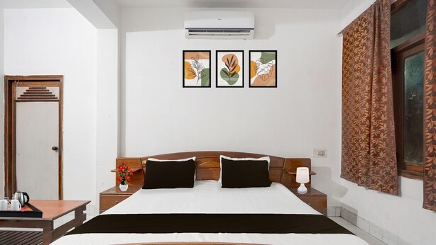 Habitación de hotel con cama de madera, mesita de noche con lámpara, aire acondicionado de pared y cuadros colgados sobre la cama.