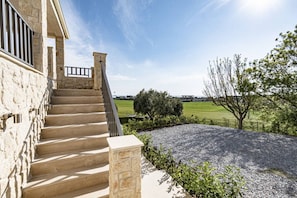 A stone staircase leading to a building with a metal railing, surrounded by a gravel area and greenery.