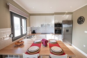 A modern kitchen with white cabinets, a stainless steel refrigerator, and a dining area set with red placemats and white plates.