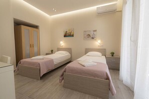 A hotel room with two beds, a desk, a wardrobe, and an air conditioning unit. - Sabbia Seafront Apartment 3 by RentalsPro (Nea Moudania)