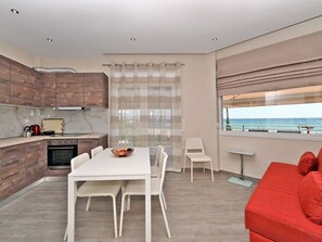 A modern kitchen with a dining area, a red sofa, and a view of the sea. - Sabbia Seafront Apartment 3 by RentalsPro (Nea Moudania)