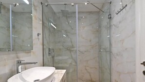 Een moderne badkamer met een glazen douchecabine, een groot wit wastafelmeubel en marmeren wanden.