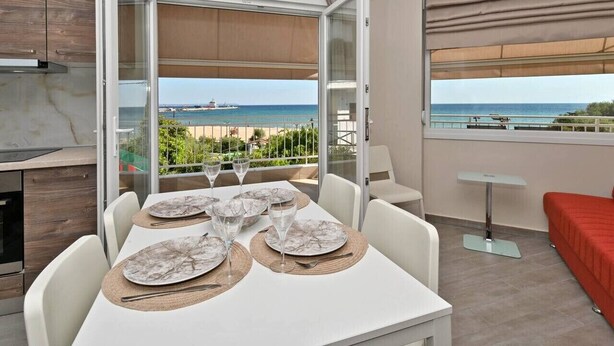 Een moderne kamer met een eettafel voor vier personen, een kitchenette en een balkon met uitzicht op zee.