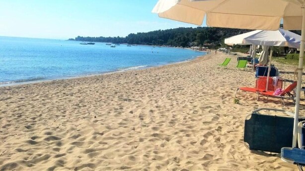 Ein Strand mit Sand, einigen Sonnenschirmen und Liegestühlen.