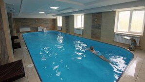 Una piscina interior con una persona nadando, paredes de azulejos y ventanas.