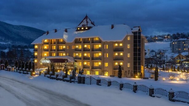 Un hotel de varios pisos con balcones, un techo cubierto de nieve y montañas al fondo.