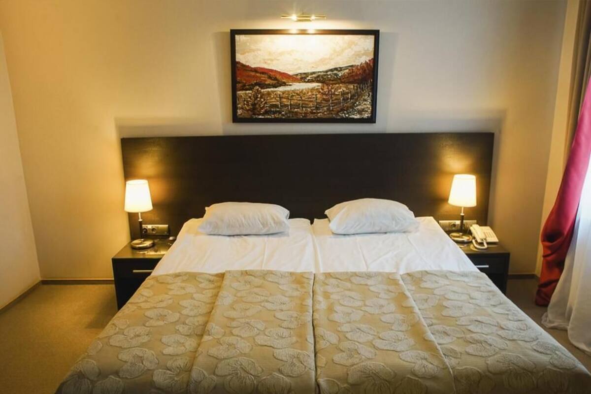 Een tweepersoonsbed met een bloemenbedekking, twee bedlampen, een nachtkastje met een telefoon, en een schilderij erboven.