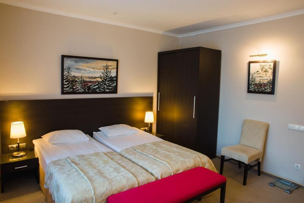 A hotel room with two beds, a wardrobe, a chair, and artwork on the walls.