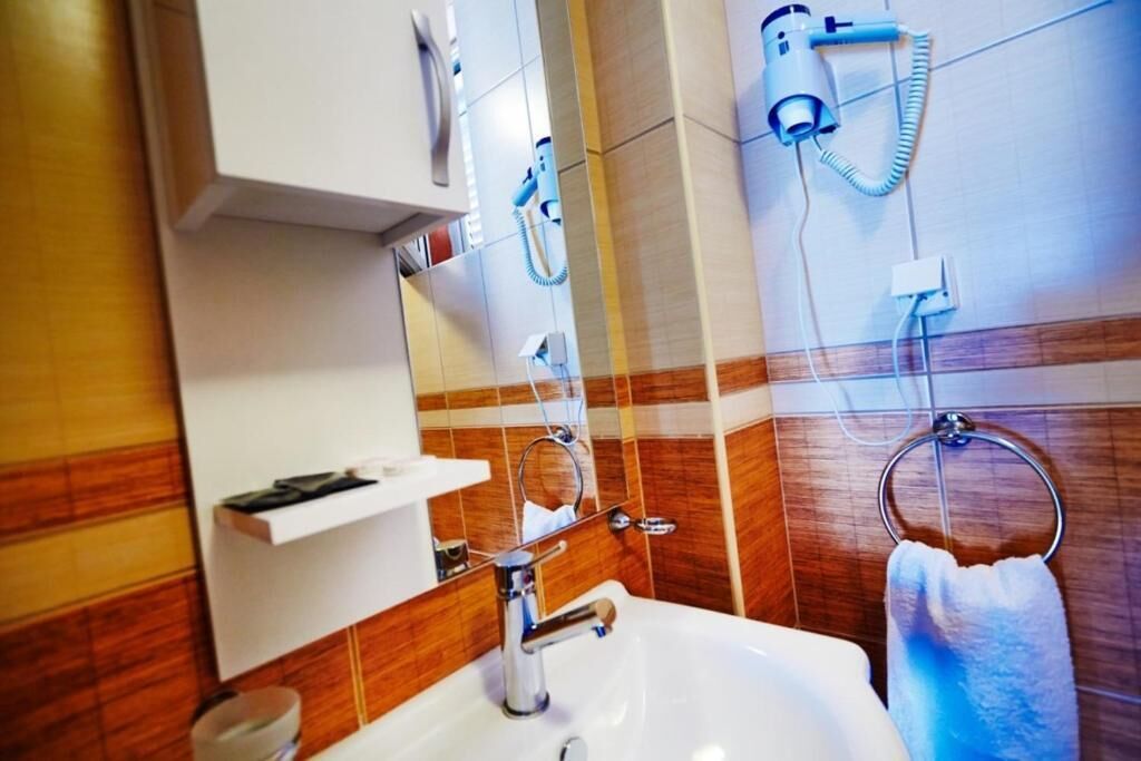Une salle de bain avec un lavabo blanc, un miroir, un porte-serviettes et un sèche-cheveux fixé au mur.